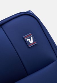 Borsa da viaggio blu navy con tessuto texturizzato. Presenta un logo rettangolare prominente con accenti rossi e argento. Design pulito e moderno.