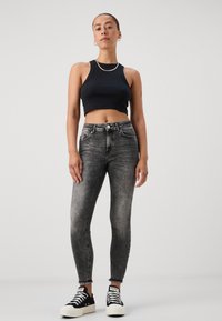 Sort cropped tank top, grå denim skinny jeans med en falmet vask, og sorte sneakers med hvide såler, der har en frynset kant.