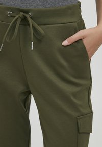 Olijfgroene sweatpants gemaakt van een zachte, gestructureerde stof. Bevat een elastische tailleband met een trekkoord en een zijzak.