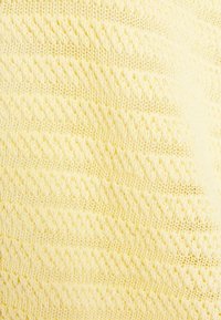 Tissu tricoté jaune doux avec un motif en maille torsadée diagonale répétée et un point filet alternant sur toute la surface.