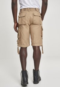 Khaki cargo shorts yang terbuat dari katun, dilengkapi dengan beberapa saku samping, tali yang dapat disesuaikan, dan potongan yang santai, dipadukan dengan sepatu bot hitam di pergelangan kaki.