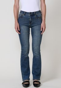 Jeans de mezclilla azules ajustados con una cintura de altura media, que presentan acentos decorativos de strass en los bolsillos frontales y un ligero desgastado en la tela.