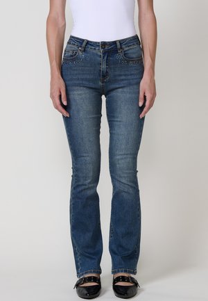 Jeans de mezclilla azules ajustados con una cintura de altura media, que presentan acentos decorativos de strass en los bolsillos frontales y un ligero desgastado en la tela.