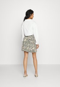 Camisa branca cortada combinada com uma saia floral com padrões em preto, amarelo e rosa. Modelo usa sandálias com salto transparente.