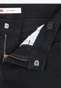 Black denim 510 Skinny jeans featuring a zipper with metallic teeth, button closure, and a white inner label. Smooth texture, fitted design.