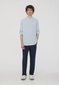 Camicia a maniche lunghe azzurro chiaro con placca con bottoni, maniche arrotolate, abbinata a pantaloni scuri e sneaker bianche. Design e vestibilità semplici.