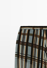 Plisseret nederdelsdel med elastisk taljebånd, der har lodrette og vandrette striber i sort, brun, grøn og blå på et gennemsigtigt stof.