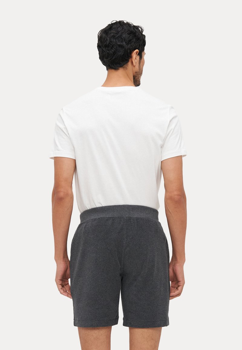 Pantaloni scurți gri din bumbac cu o textură moale și talie elastică, purtați cu un tricou alb, văzuți din spate pe un fundal neutru.
