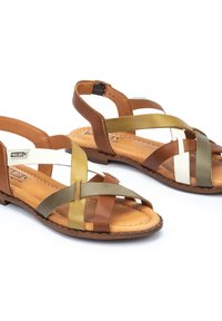 Sandali in pelle marrone e multicolore con fasce incrociate di colore marrone, verde e bianco. Sole piatto con cinturino posteriore e soletta imbottita.