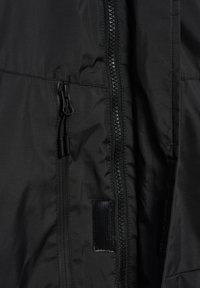 Czarna tekstylna kurtka z wyraźnym zapięciem na zamek, regulowanymi uchwytami i miękką, gładką fakturą bez widocznych wzorów.