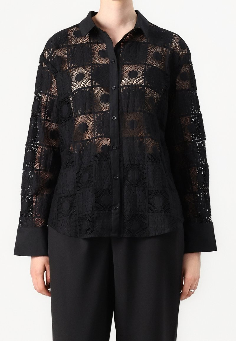 Svart spetstopp med rutmönster, med långa ärmar och knappframsidan, kompletterad med en solid svart krage och manschetter.