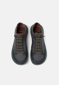 Sneaker grigie scure con tessuto testurizzato, suola in gomma verde e lacci marroni. Presentano il marchio Campeer sulla linguetta e sul lato.