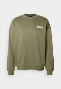 Olive zielona bluza z długim rękawem i okrągłym dekoltem, z żebrowanymi mankietami i dołem, z małym białym logo "HUGO" na górnej lewej części klatki piersiowej.