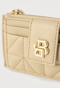 Bézs bőr pénztárca párnázott mintával, több kártyatartóval, aranyszínű fémalkatrészekkel és cipzáras záródással. Kiemelkedő logó díszítés.