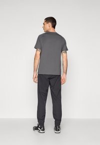 Grå t-shirt med korte ærmer parret med sorte joggers. Joggersne har elastiske manchetter og en glat tekstur. Fodtøjet er sort med hvide accenter.