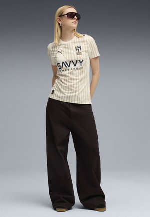 Beige gestreiftes Sportshirt mit Logo, runder Halsausschnitt, kombiniert mit schwarzen weit geschnittenen Hosen und Sonnenbrille. Glatter Stoff, lässige Passform.