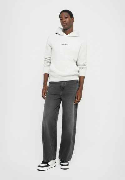 Hoodie gris avec une poche sur le devant et un logo ; associé à un jean large foncé et des baskets noir et blanc. Textures lisses dans l'ensemble.