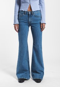 High-waisted blue denim flared jeans featuring a faded texture, classic five-pocket design, and subtle stitching details.