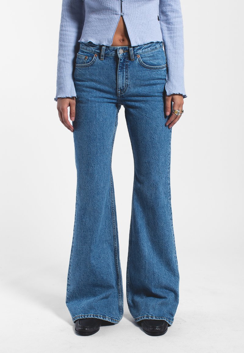 High-waisted blue denim flared jeans featuring a faded texture, classic five-pocket design, and subtle stitching details.