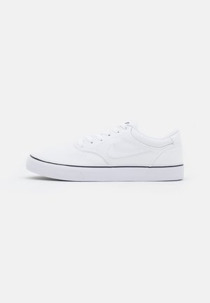 Biały niski sneaker Nike ze sznurowaniem i czarnym paskiem na białej gumowej podeszwie, pokazany na jednolitym jasnoszarym tle.
