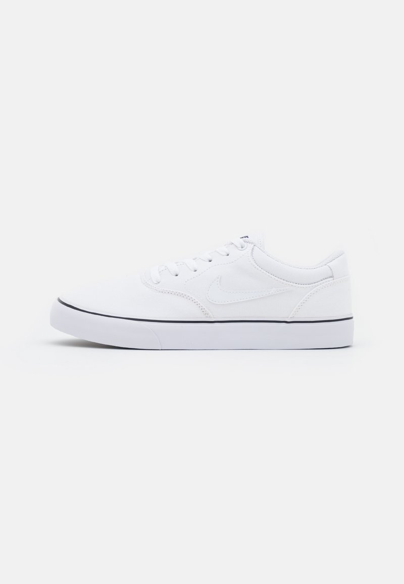 Sneaker Nike blanc basse avec fermeture à lacets et bande noire sur la semelle en caoutchouc blanche, présenté sur un fond gris clair uni.