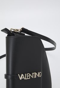Černá kožená kabelka se strukturovaným siluetou, obsahující zlaté logo "VALENTINO", tenký řemen a elegantní design.