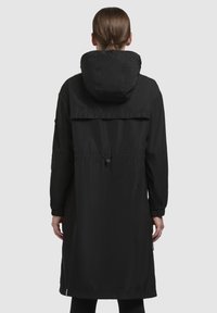 Lang zwarte regenjas met een capuchon, elastische manchetten en een verstelbare taille. Gemaakt van lichtgewicht waterdicht materiaal, met een subtiele glans en een rechte zoom.