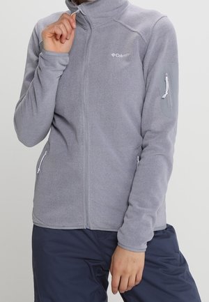 Hellgraue Fleecejacke mit Frontreißverschluss, Reißverschlusstaschen an Hüften und Ärmel, getragen von einer Person, die den Kragen anpasst.