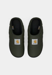 Et par mørkegrønne polstrede slip-on tæpper, med sort inderside og Carhartt logo-patch på toppen, set ovenfra.