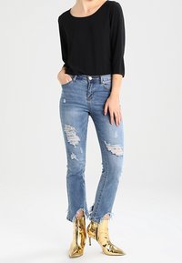 Svart topp med trekvartsärm, kombinerad med slitna ljusblå jeans med fransar och blanka guldankelstövlar.