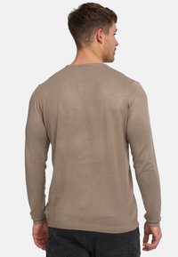 Maglione marrone a maniche lunghe con texture a costine, scollatura a girocollo e polsini aderenti. La vista dal retro mostra una finitura liscia e dettagli minimal.