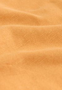 Tissu en coton d'une douce teinte orange, affichant une texture subtile avec de légères rides et une surface lisse.