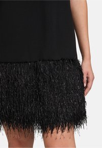 Czarna sukienka z fakturowym frędzlem na dolnej krawędzi, w którym znajdują się metaliczne nici. Górna część jest gładka, a frędzle są długie i puszyste.