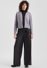 Jasnoszary krótki kardigan z długimi rękawami, wykonany z fakturowanej tkaniny, z rozpiętym przodem, zestawiony z czarnymi spodniami o szerokich nogawkach oraz małą czarną torebką.