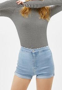 Svartvitt randig långärmad topp med hög halsringning, kombinerad med figurnära ljusblå denimshorts med knappstängning och uppvikt fåll.