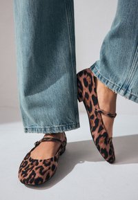 Ballerines imprimé léopard avec bout arrondi, confectionnées en tissu doux, dotées d'une fine lanière sur le cou-de-pied, associées à un jean bleu clair.