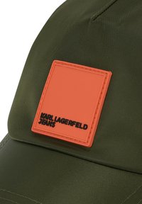 Olivazöld sapka narancssárga négyzet alakú folttal, amelyen fekete színben van belegravírozva a "KARL LAGERFELD JEANS" felirat. Tartós anyagból készült, texturált felülettel.
