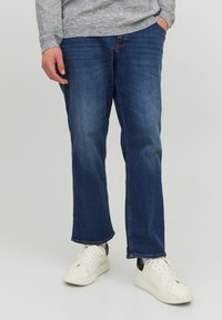 Blauwe denim jeans met een rechte pijp ontwerp, subtiele vervaging en contrasterende stiksels, gedragen met witte sneakers met een donkere accent.