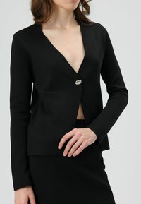 Zwarte gebreide cardigan met lange mouwen, diepe V-hals en zilverkleurige knoopsluiting. Heeft een gladde textuur en een rechte snit.