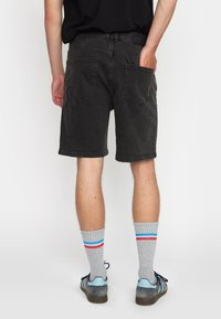 Zwarte denim shorts met achterzakken, onafgewerkte zoom en subtiele vervaging. Gepaard met grijs gestreepte sokken en blauwe sneakers.