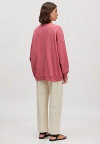 Roze sweatshirt met verlaagde schouders, voorzien van geribde manchetten en onderkant, gecombineerd met crèmekleurige wijde broek en zwarte sandaal.