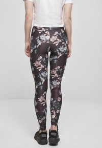Leggings visoke struka izrađene od rastezljivog materijala sa cvjetnim uzorkom u ružičastoj, plavoj i zelenoj boji na tamnoj pozadini. Nosene crne patike.