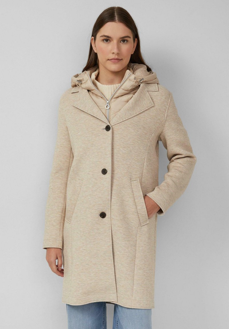 Beige jas met een capuchon, gemaakt van een gestructureerde stof, met een grote kraag en vijf knopen. Inclusief twee zijzakken en een ritssluiting aan de binnenkant.