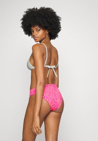 Top de bikini cinza em forma de triângulo com detalhe de laço nas costas e parte de baixo de cintura alta em estampa de onça rosa, apresentando uma textura suave e cores vibrantes.