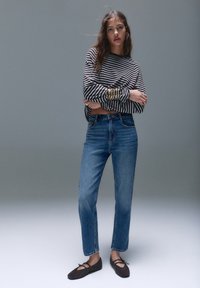 Gestreiftes Langarmshirt in Schwarz und Weiß, hochgeschnittene blaue Jeans und dunkelbraune Ballerinas. Weicher Stoff, lockere Passform und verkürztes Design.