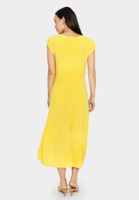 Yellow cap-sleeve dress in lightweight fabric. Flowing silhouette with a knee-length hem. Smooth texture and subtle seam detailing at the back.