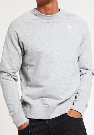 Sweat à capuche gris avec un col rond, des manches raglan, des poignets et un bas côtelés, présentant un petit logo Nike blanc sur la poitrine.