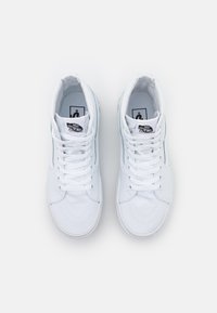Zapatillas altas blancas con parte superior de lona, cordones planos y suelas de goma. Presentan un parche de logo negro en la lengua y detalles de costura.