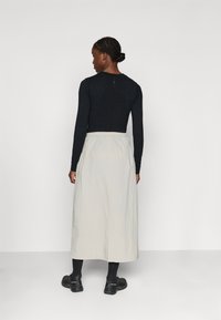 Long, light grey skirt with an elastic waistband paired with a fitted black long-sleeve top. The ensemble has a simple, modern design.