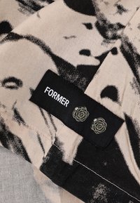 Black-and-beige fabric with abstract print; black label reading "FORMER" and two small glass rose-shaped embellishments. Cotton texture.